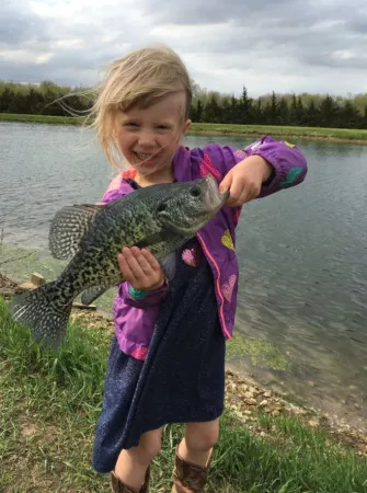 child smiling and holding a fish while fishing at a pond